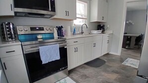Een keuken met witte kastjes, een fornuis, een spoelbak en een koelkast.