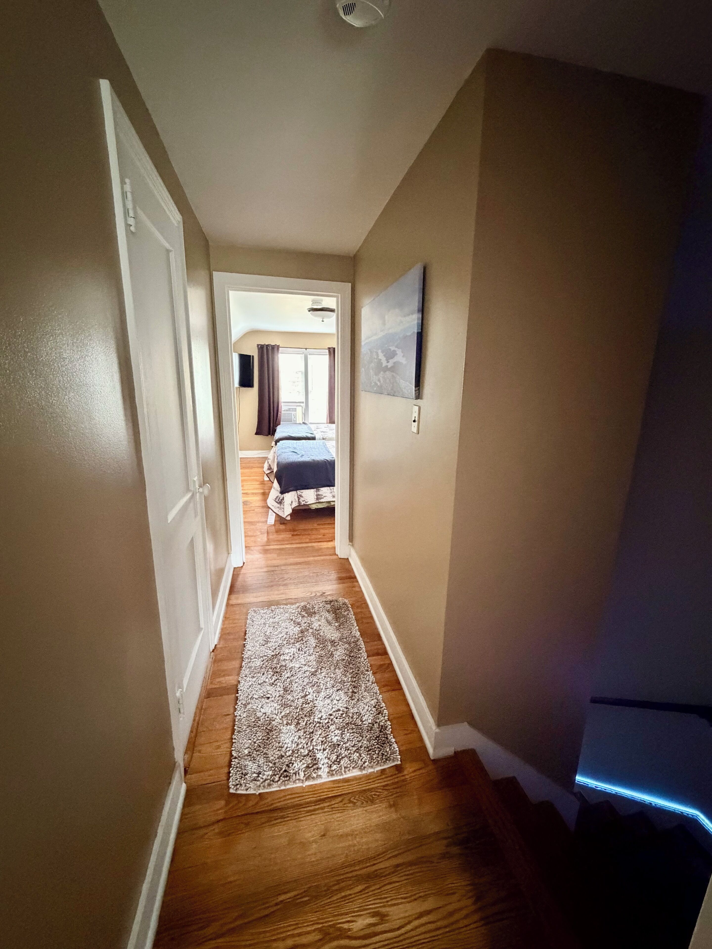 Um corredor com assoalho de madeira, tapete, porta e escada com luz azul.