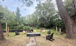 An outdoor seating area with chairs and a table, surrounded by trees. - Spacious Country Retreat – Perfect for Families, Groups & Getaways (Plattsburgh)
