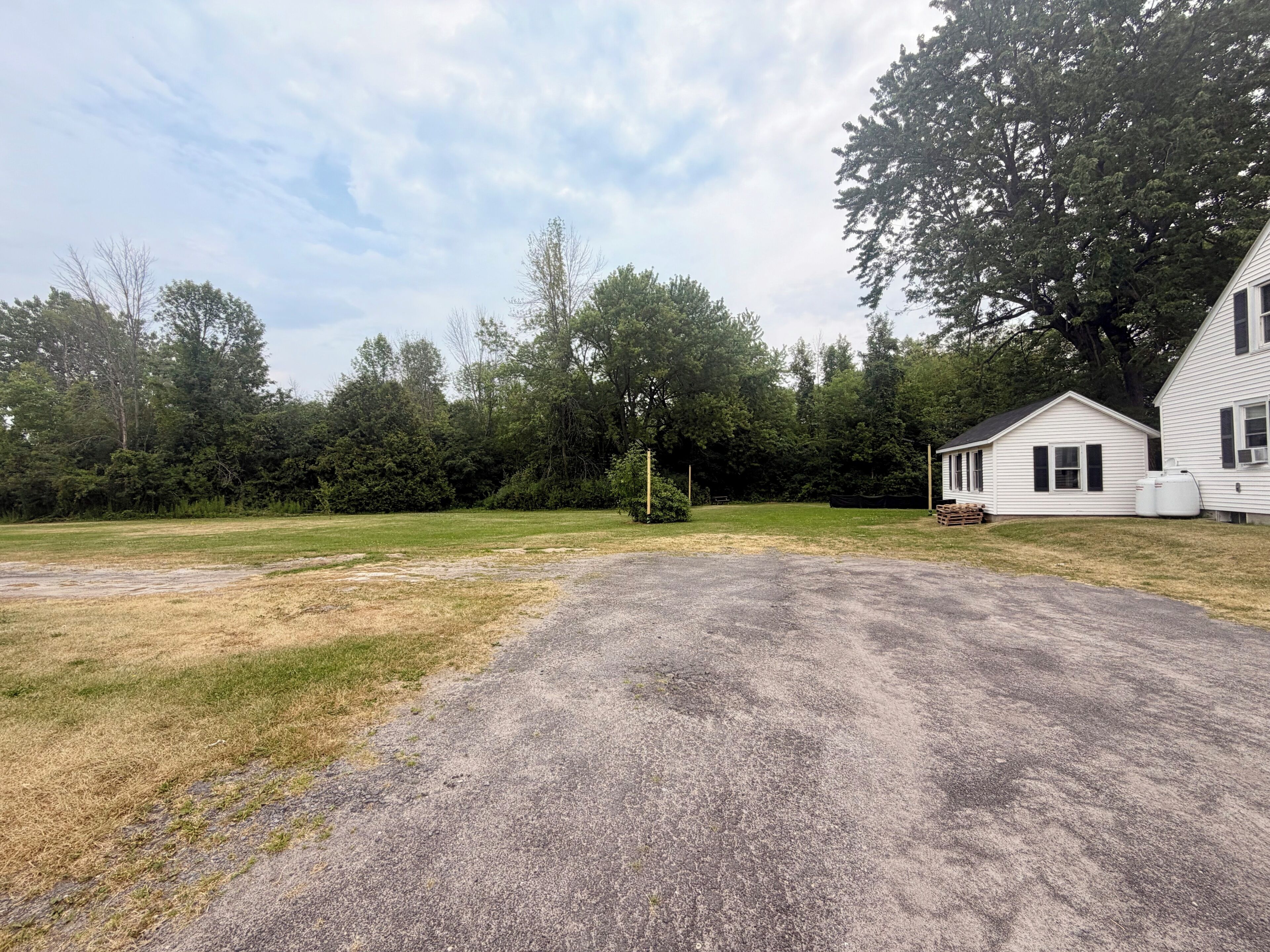 Une propriété située en zone rurale, avec une allée en gravier, une petite maison blanche et des arbres tout autour.