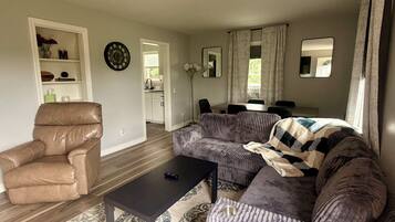 A living room with a brown leather chair, a black coffee table, a patterned rug, and a grey sofa with a blanket.