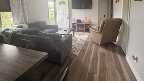 Een woonkamer met een bank, een eettafel en een aan de muur bevestigde televisie.