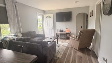 A living room with a sofa, a dining table, and a TV mounted on the wall.