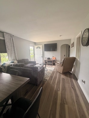 A living room with a sofa, a dining table, and a TV mounted on the wall. - Spacious Country Retreat – Perfect for Families, Groups & Getaways (Plattsburgh)