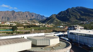 A building with a flat roof, a parking area, and a mountainous landscape in the background. - Bright apartment in Los Llanos downtown (Los Llanos)