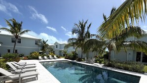 En swimmingpool med solstolar, palmer och en byggnad med vit fasad.