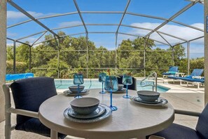 A covered outdoor seating area with tables and chairs, a pool, and lounge chairs. - Saltwater Pool-Windsor Palms Resort, Backing Conservation Area-6 Miles to Disney (Kissimmee)
