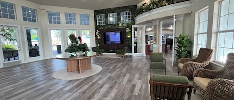 Un hall d’entrée spacieux doté d’un plancher en bois, de coins salon, d’un comptoir de réception et de grandes fenêtres.