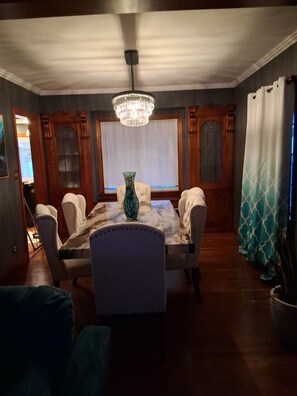 Un comedor con candelabro, paneles de madera y un gran ventanal con persianas.