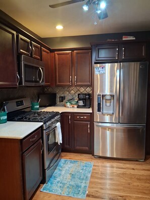 Una cocina con armarios de madera, electrodomésticos de acero inoxidable, un microondas, una estufa y un refrigerador.