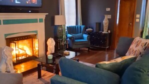Un salon avec une cheminée, un téléviseur, un ventilateur de plafond et un fauteuil bleu.