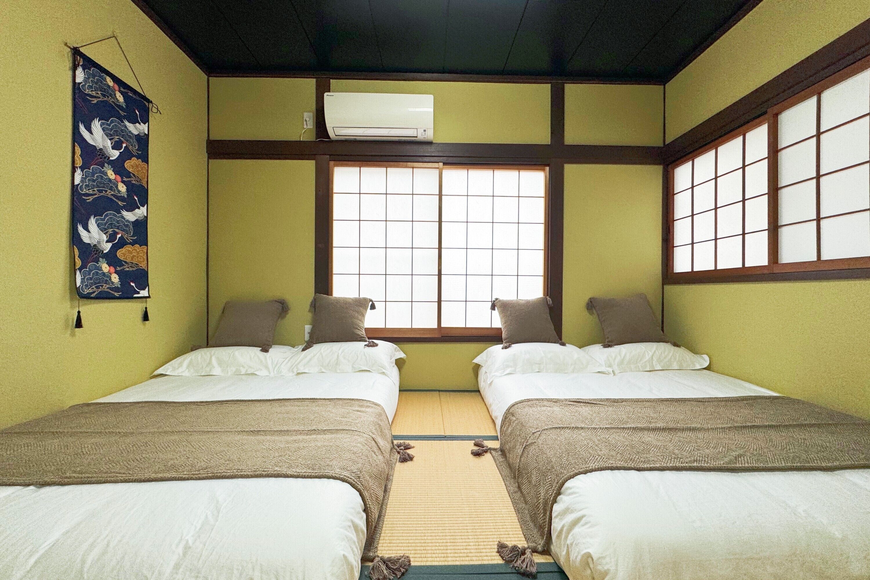 A traditional Japanese-style room with two beds, tatami flooring, shoji screens, and an air conditioning unit.
