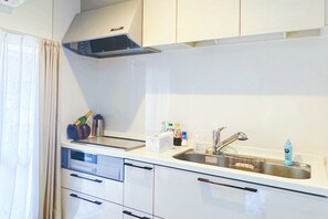 Una cucina compatta con mobili bianchi, un lavello in acciaio inossidabile e una cappa aspirante.