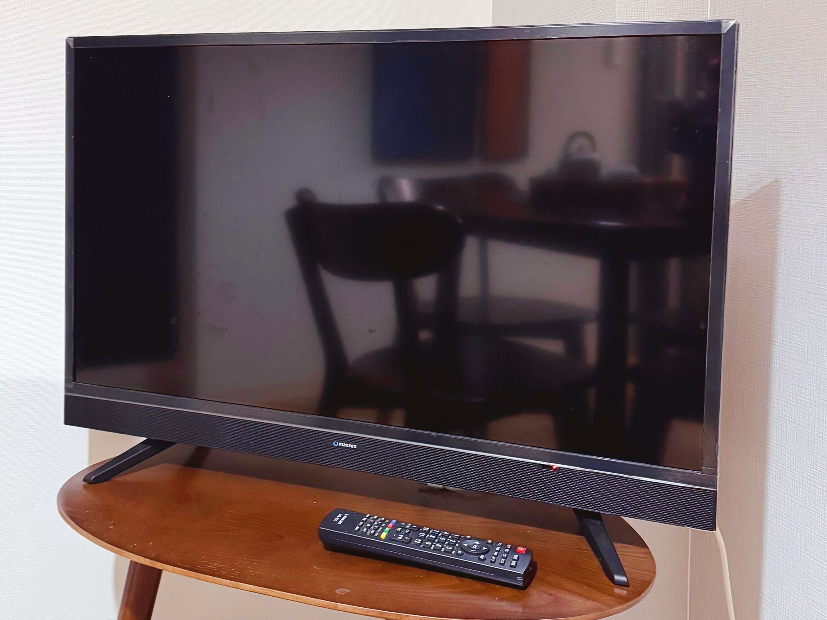 A television on a stand with a remote control on a wooden table.