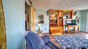 Una sala de estar con un sofá, un televisor sobre un mueble de madera, un tapete estampado y una zona de comedor visible a través de una puerta abierta.