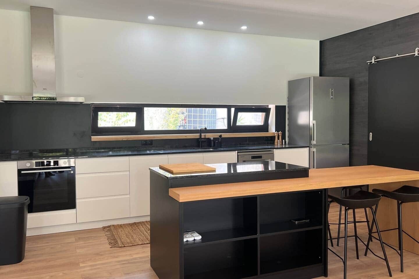 A modern kitchen with a central island, black cabinetry, and a large refrigerator.