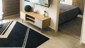 Una sala de estar moderna con un televisor de pantalla plana, un mueble de madera, una planta pequeña y una cama al fondo.