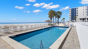Une piscine avec vue sur la plage, des chaises longues et des palmiers.