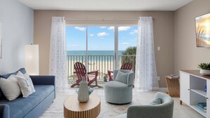 Un salon comprenant un canapé, des fauteuils, une table basse et offrant une vue sur la plage grâce à de grandes fenêtres.