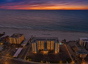 A hotel with multiple floors, a parking lot, and a view of the ocean at sunset. - An Ocean Breeze puts a Mind at Ease (Madiera Beach)