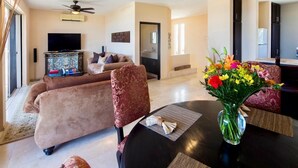 A living room with a sofa, a dining table with a vase of flowers, a television, and a ceiling fan.