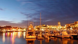 A marina with boats docked, a prominent tower, and buildings with warm lighting.