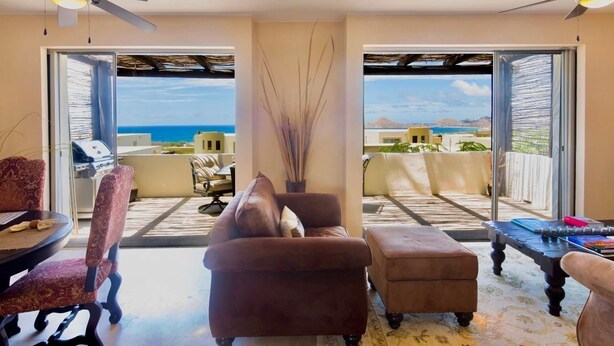 A room with a sofa, armchairs, a dining table, and a view of the ocean through large sliding doors.