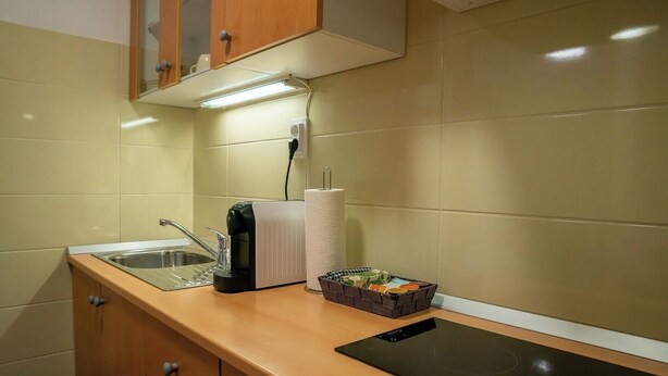 A kitchen with a sink, a toaster, a kettle, a box of tea bags, and a black induction cooktop. - Small and cozy apartment｜Free parking (Maribor)