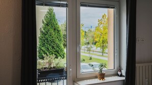 A window with a view of a road and trees, a potted plant on the sill, and a gnome decoration. - Small and cozy apartment｜Free parking (Maribor)