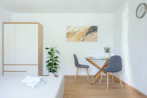 A room with a bed, a desk with two chairs, a plant, and a painting on the wall. - Small and cozy apartment｜Free parking (Maribor)