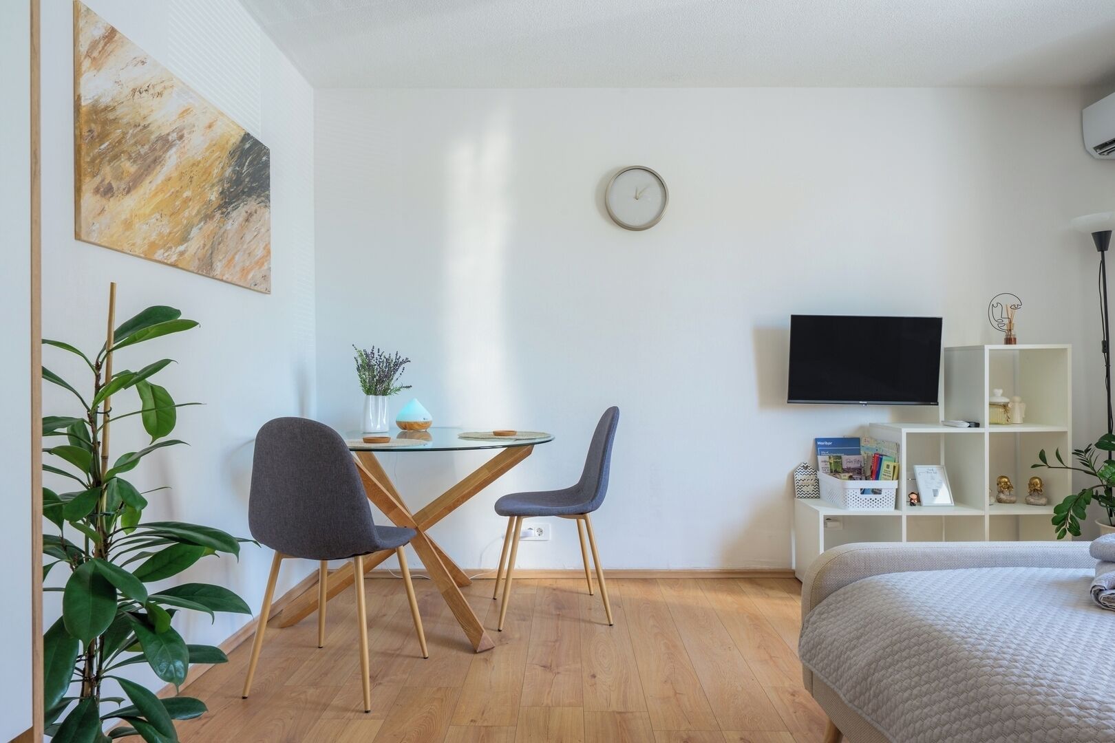Een moderne slaapkamer met een bed, een televisie, een bureau met stoelen en een plant.