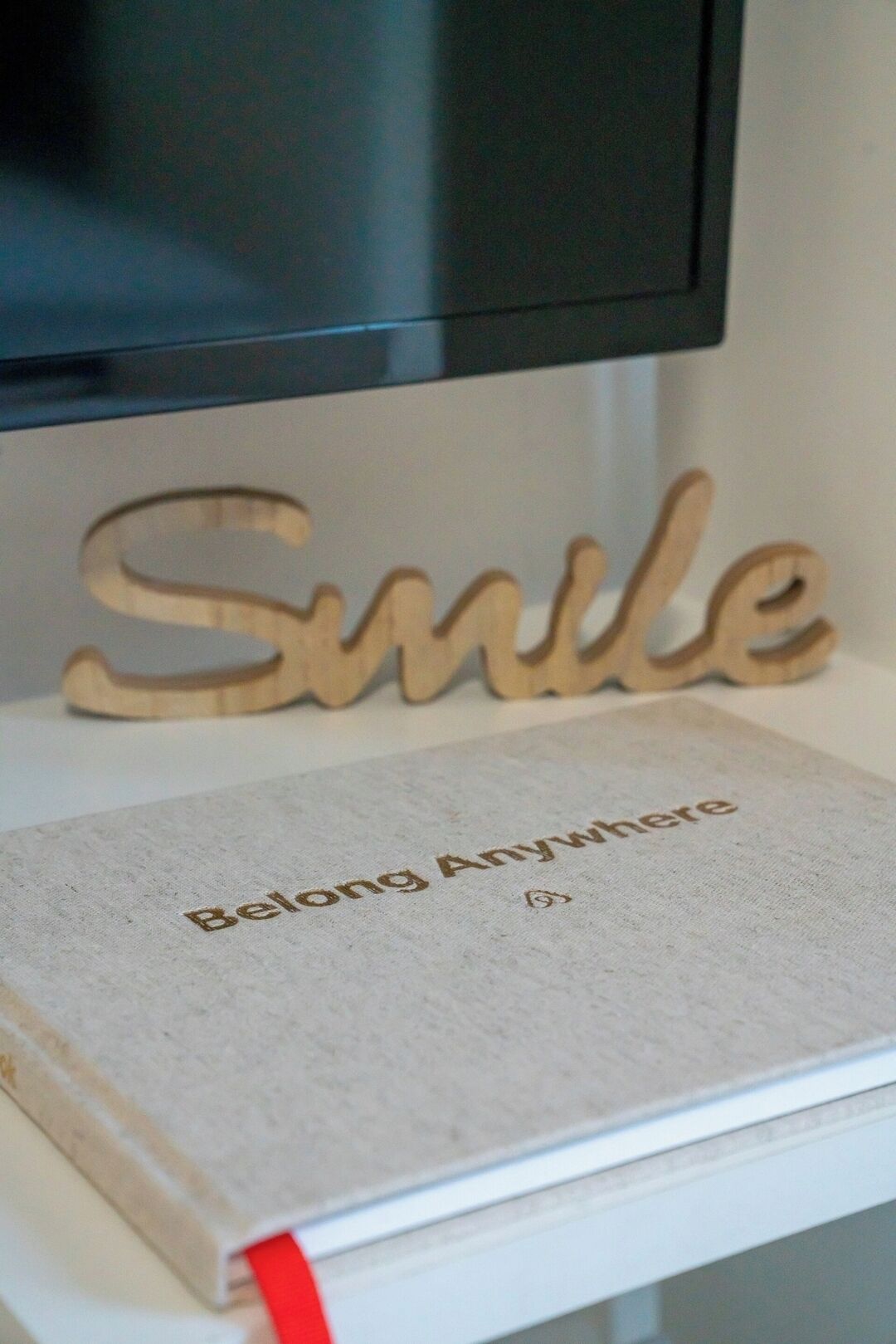 Een boek met de titel 'Belong Anywhere' op een wit oppervlak, met een houten bord waarop 'Smile' staat.