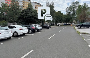 A parking lot with multiple cars, a large building in the background, and a sign indicating parking availability.