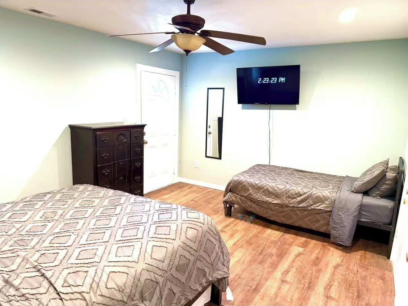 Un dormitorio con dos camas, ventilador de techo, televisor y cómoda.