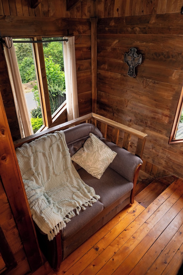 A cozy wooden cabin room with a brown sofa, a white throw blanket, and a wooden bench.