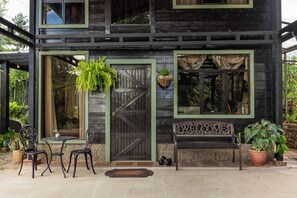 Une maison en bois avec une porte d’entrée, deux fenêtres, un banc et un pot de fleurs.