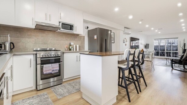 Una cocina moderna con electrodomésticos de acero inoxidable, una isla central y una zona de comedor con taburetes de bar.