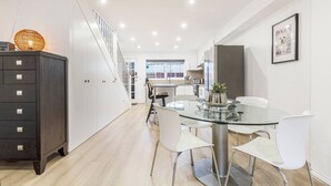 Una cocina moderna con una mesa de comedor de vidrio, sillas blancas y un armario de madera oscura.