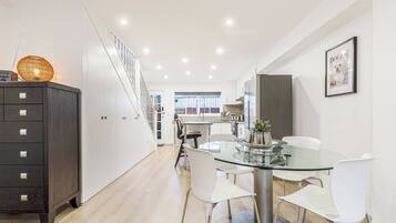 A modern kitchen with a glass dining table, white chairs, and a dark wooden cabinet.