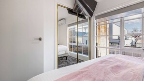 Un dormitorio con una cama, un ventanal grande y un televisor montado en la pared.