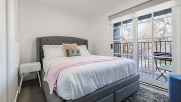 A bedroom with a bed, nightstand, and a view of the outside.