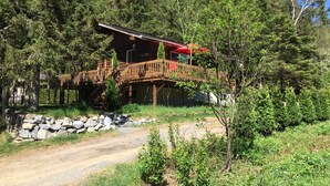 A cabin with a wooden deck and a red umbrella, surrounded by dense forest. - Chalet Du Nord (Saint-Adolphe-d'Howard)