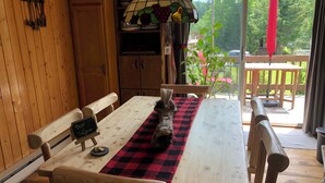A wooden interior with a table and benches, a hanging light fixture, and a view of the outdoors. - Chalet Du Nord (Saint-Adolphe-d'Howard)