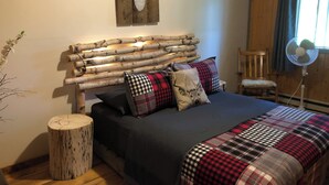 A bedroom with a log headboard, plaid bedding, and a mounted deer head. - Chalet Du Nord (Saint-Adolphe-d'Howard)