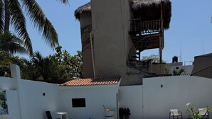 A swimming pool with a metal ladder, lounge chairs, and a thatched-roof structure.
