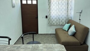 A room with a brown sofa, a dining table, a ceiling fan, a door, and a window with floral curtains.