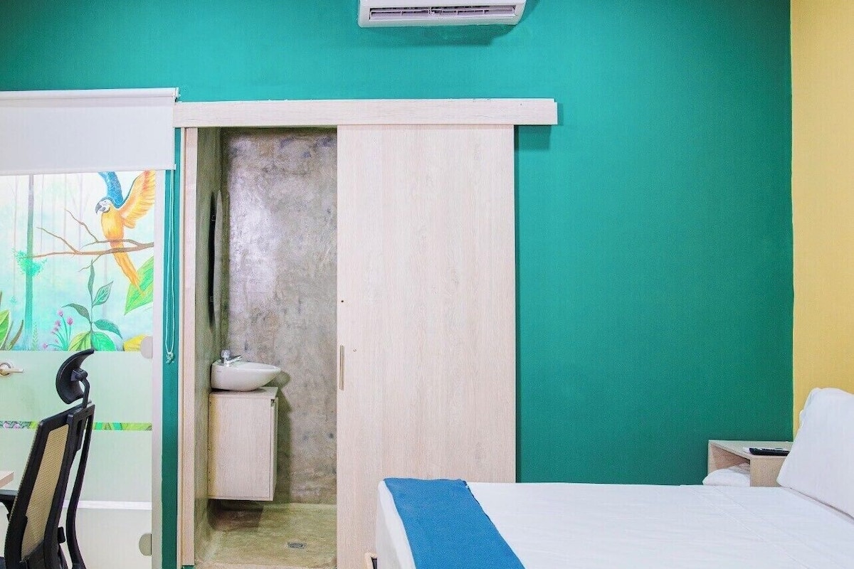 A hotel room with a bed, a desk, a chair, an air conditioner, and a bathroom.