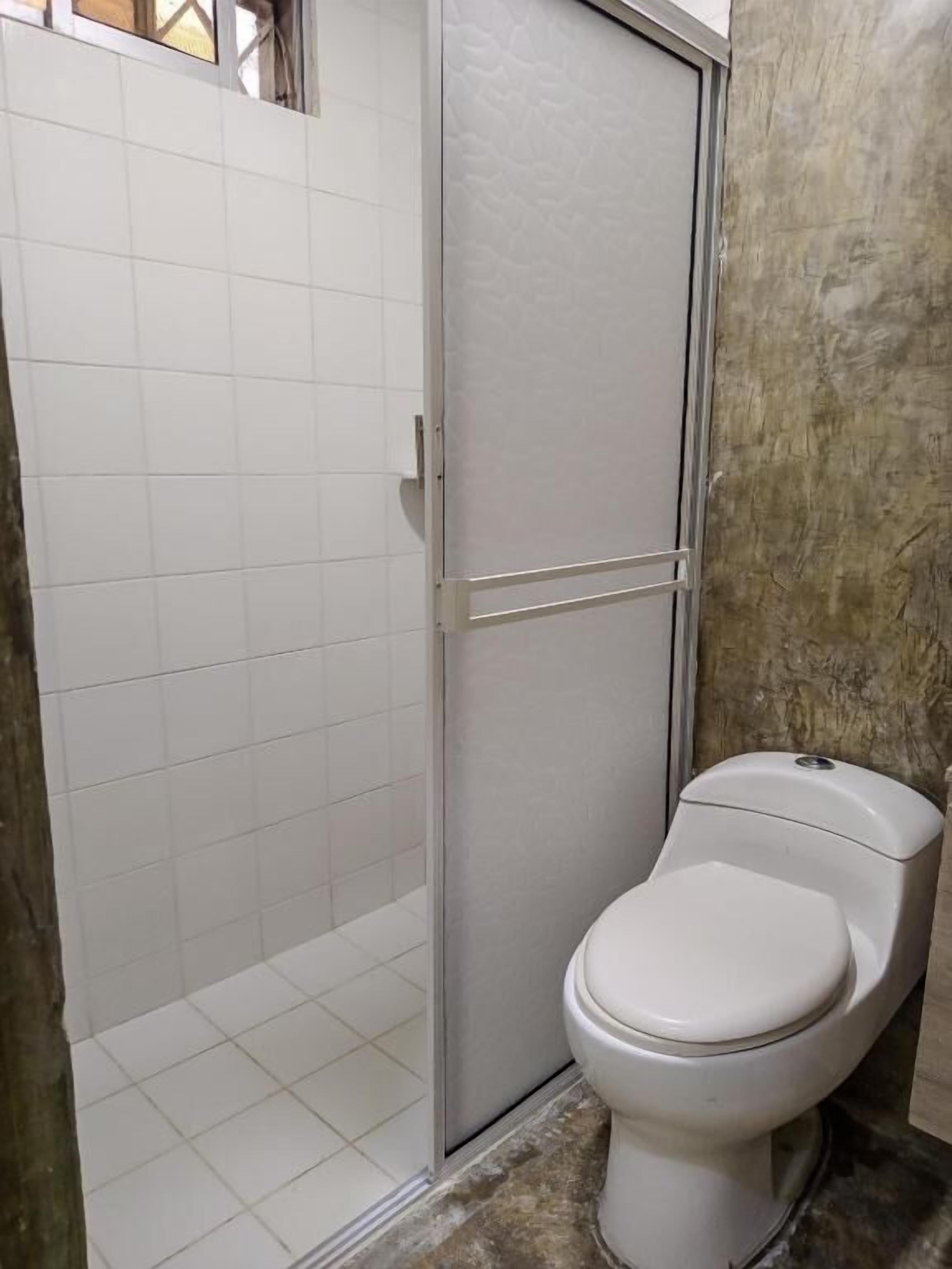 A bathroom with a toilet, a shower enclosure, and tiled walls.