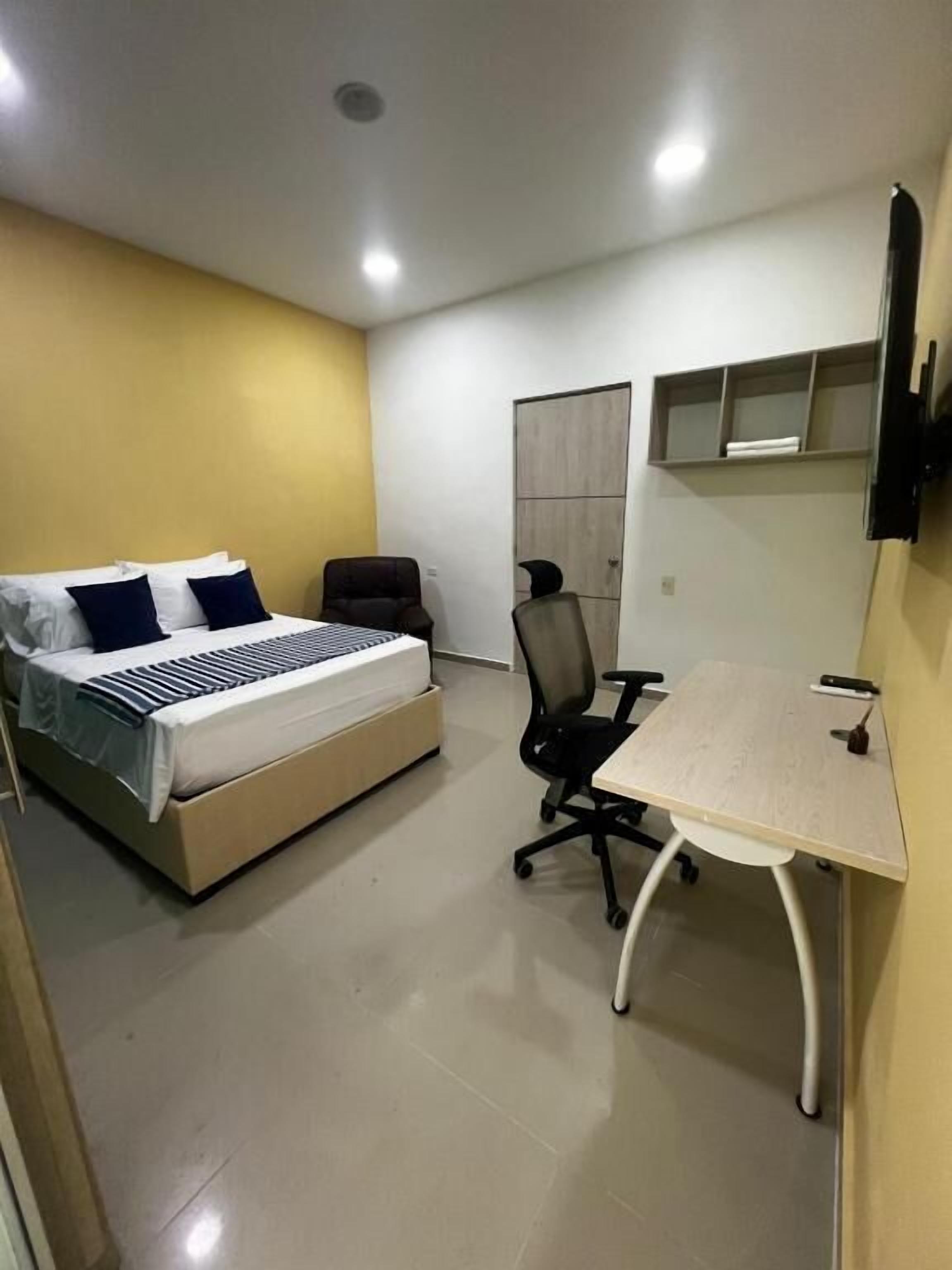 A bedroom with a bed, a desk, a chair, a wardrobe, and a television.
