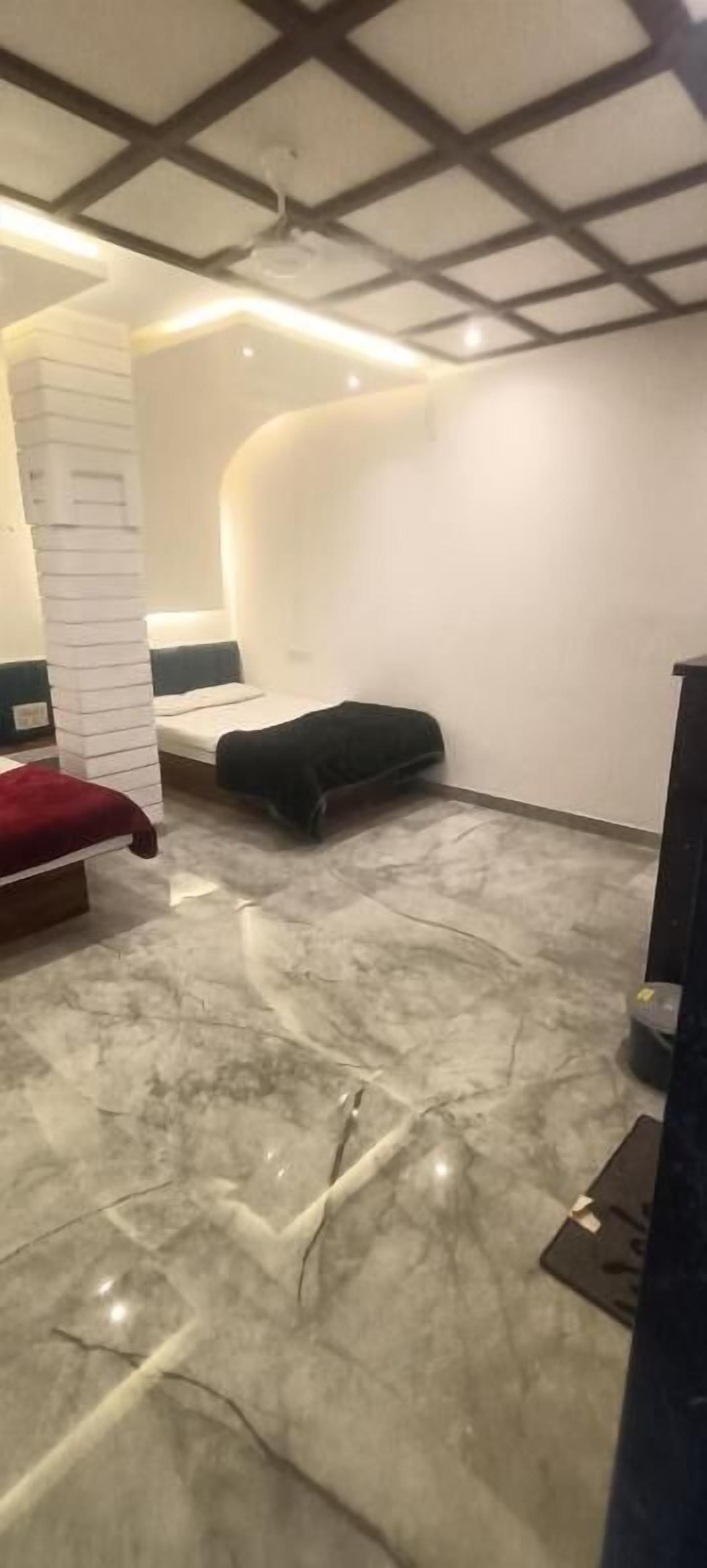 A room with a marble floor, a bed with a red headboard, a black ottoman, and a white pillar.